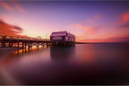 Busselton Pier with houses at sunset on a calm water surface