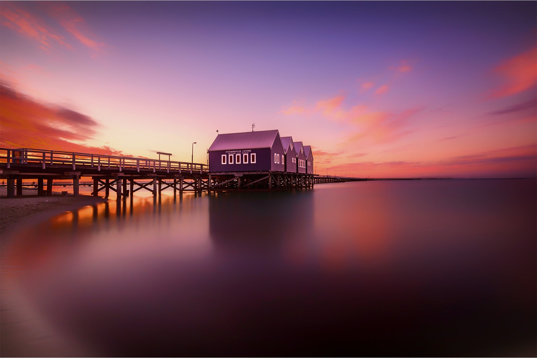 Busselton Pier with houses at sunset on a calm water surface