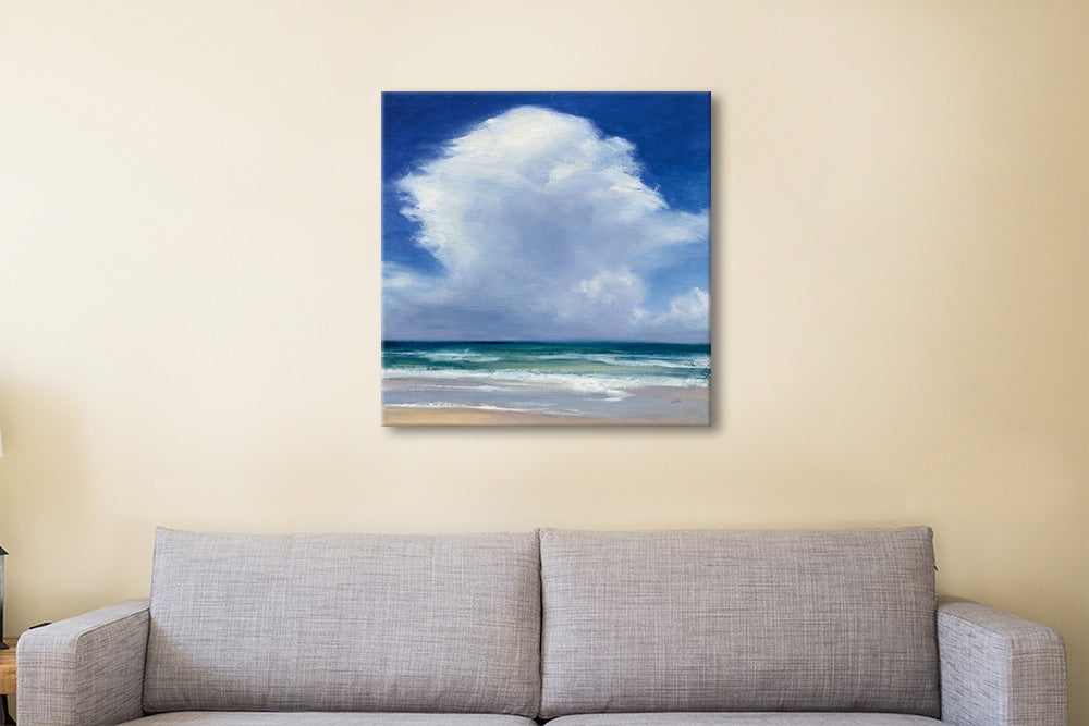 Canvas print of a beach scene with a large cloud hanging above the ocean, displayed on a wall above a sofa.